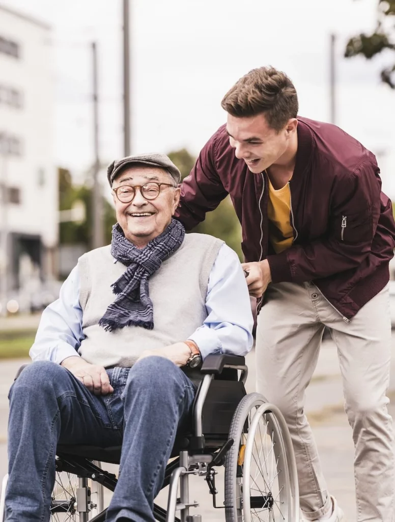 Lachender junger Mann schiebt einen lachenden Senioren auf einem Rollstuhl